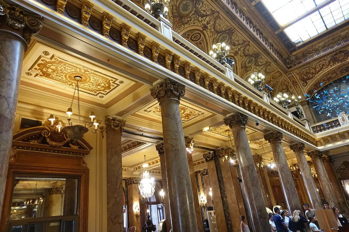 Visitors in ordinary summer clothes standing under the marble colonnade and gilded upper gallery of the Casino de Monte-Carlo atrium
